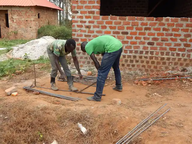 Two workers bending steel reinforcement beside a brick wall on a building site