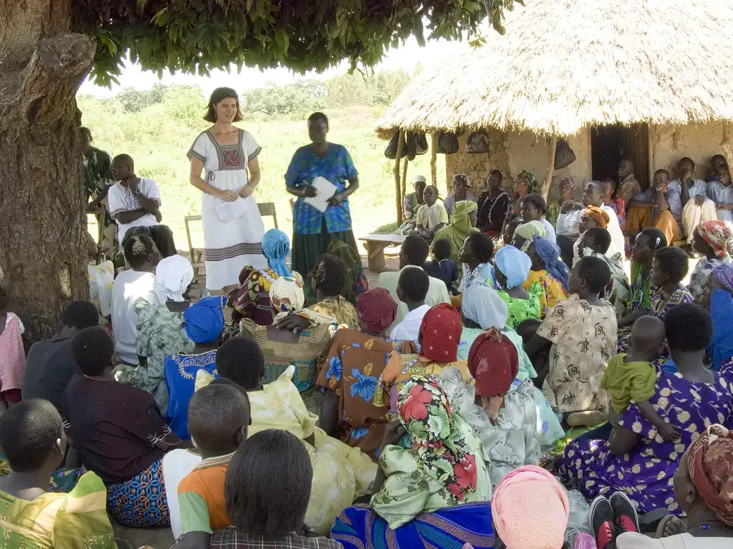 A women's group meeting under a thatched shelter